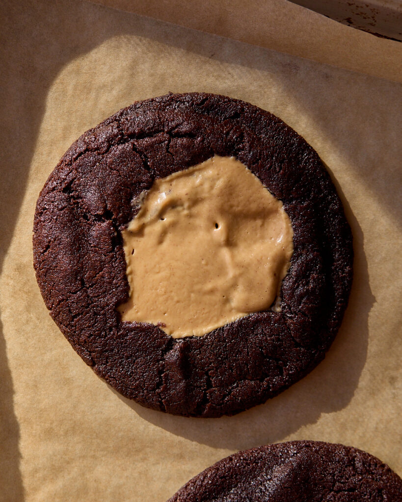 A chocolate cookie with gooey peanut butter filling on a parchment lined baking sheet
